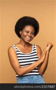 Studio portrait of smiling young black woman with curly hair isolated on beige background. Beautiful african american female model wearing striped t-shirt with crossed arms. Positive emotion . Studio portrait of smiling young black girl with curly hair isolated on beige wall. Positive emotion