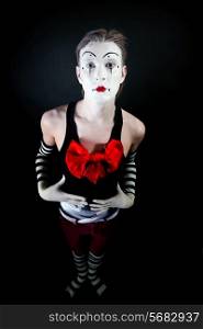 Studio portrait of theatrical funny clown with a big red bow on the chest on a black background