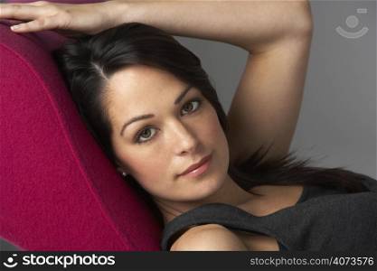 Studio Portrait Of Woman Relaxing On Pink Chaise Longue