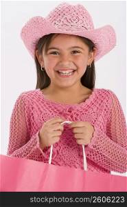 Studio portrait of young girl wearing pink cowgirl hat and carrying pink shopping bag