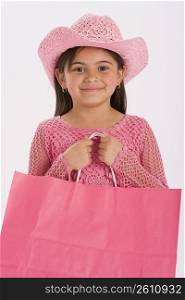 Studio portrait of young girl wearing pink cowgirl hat and carrying pink shopping bag