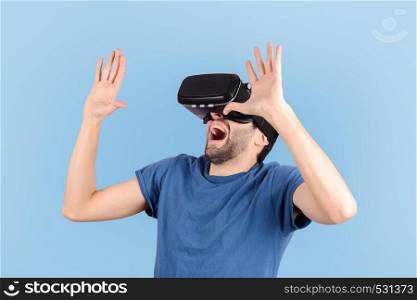 Studio portrait of young guy with VR headset is looking at interactive screen. Man experiencing virtual reality on blue background.