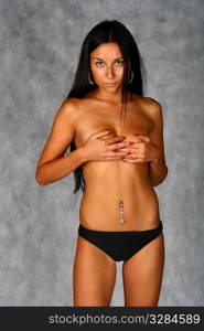 Studio shoot of a young girl in panties shirtless. Covers breasts with hands.