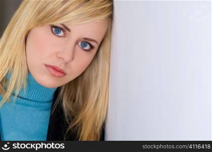 Studio shot of a beautiful blond haired blue eyed woman dressed smartly leaning against a white wall and looking thoughtful. Shot with copy space.