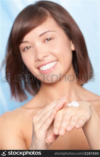 Studio shot of a beautiful Oriental young woman applying moisturising cream to her hands. The focus is on her hand and the cream in the foreground