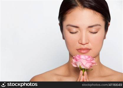 Studio shot of a beautiful young Japanese woman holding a pink rose between her clasped hands while in meditative contemplation