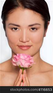 Studio shot of a beautiful young Japanese woman holding a pink rose between her clasped hands