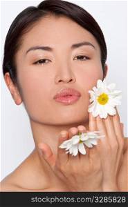 Studio shot of a beautiful young Japanese woman holding daisies and blowing a kiss to the camera.