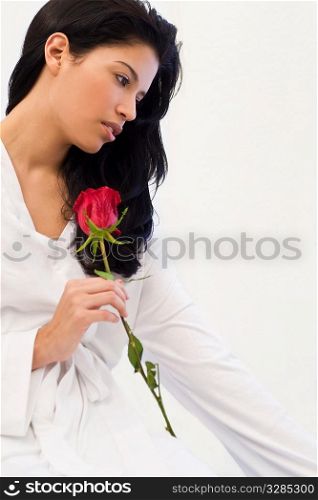 Studio shot of a beautiful young Latina woman dressed in a white robe, looking thoughtful and holding a rose
