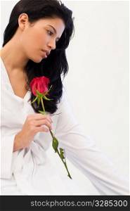 Studio shot of a beautiful young Latina woman dressed in a white robe, looking thoughtful and holding a rose