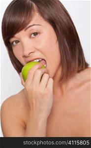 Studio shot of a beautiful young woman bitong into a juicy green apple