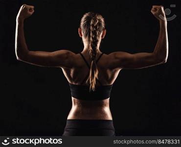 Studio shot of a fit young woman showing her muscles, against a dark background