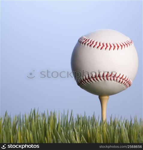 Studio shot of baseball resting on golf tee in grass.