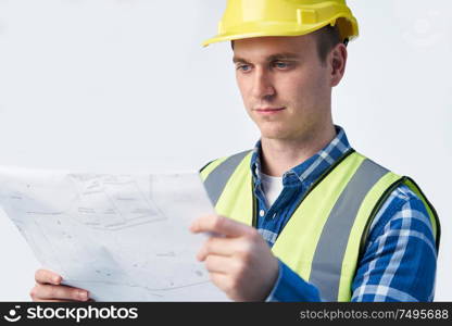 Studio Shot Of Builder Architect Looking At Plans Against White Background