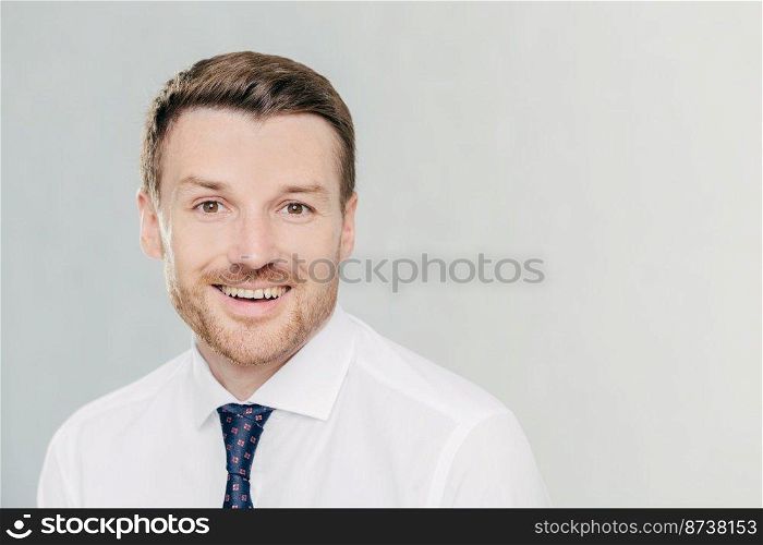 Studio shot of handsome unshaven male entrepreneur with cheerful expression, rejoices raising sales, dressed in formal clothes, isolated over white background with copy space aside for your text