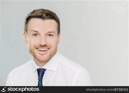 Studio shot of handsome unshaven male entrepreneur with cheerful expression, rejoices raising sales, dressed in formal clothes, isolated over white background with copy space aside for your text