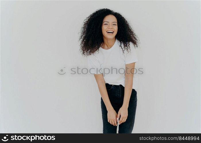 Studio shot of joyful African American woman laughs happily, dressed in casual wear, feels good, poses against white background with blank space for your advertising content, feels energized