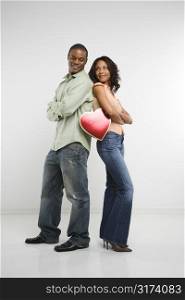Studio shot of multi-ethnic couple standing back to back with arms crossed smiling and holding valentine heart.