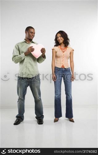 Studio shot of multiethnic couple giving each other valentine heart.