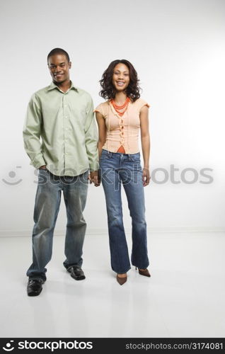 Studio shot of multiethnic couple holding hands smiling and looking at viewer.