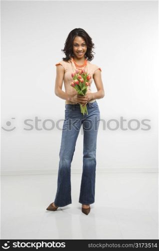 Studio shot of multiethnic mid-adult stylish woman holding bouquet of tulips smiling and looking at viewer.