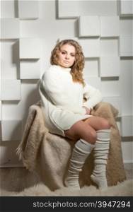 Studio shot of sexy woman in long socks and sweater posing on chair