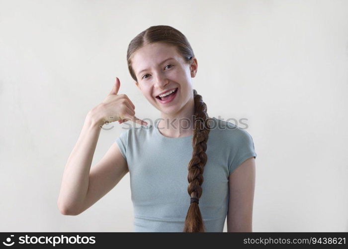 Studio Shot Of Smiling Teenage Girl Making Call Me Gesture Looking Into Camera