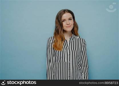 Studio shot of smiling young woman wearing casual clothes feeling relaxed and having happy expression while posing against blue background in studio, happy teenage girl expressing good emotions. Happy teenage girl expressing good emotions while posing against blue background