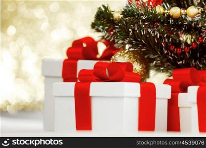 Studio shot of white gifts with red ribbons under Christmas tree, on bokeh background