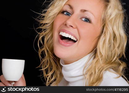 Studio shot on a black background beautiful young blond woman wearing white, laughing and drinking coffee.