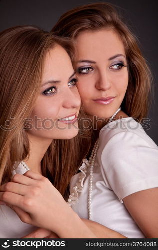 studio shot portrait on isolated background of two sisters twin women friends holding in arms each other