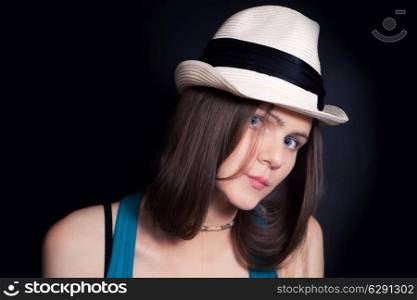 Studio shoulder portrait of young blue-eyed girl in white hat on black background