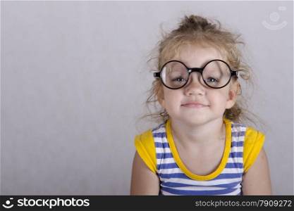 Studio, two-year-old girl sitting on the table, covered with a white cloth, and looking at the picture. Girl dressed funny glasses, hands laid on my knees