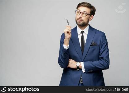 Studuo shot of thinking solving problem businessman wearing suit holding pen over grey background. Studuo shot of thinking solving problem businessman wearing suit holding pen