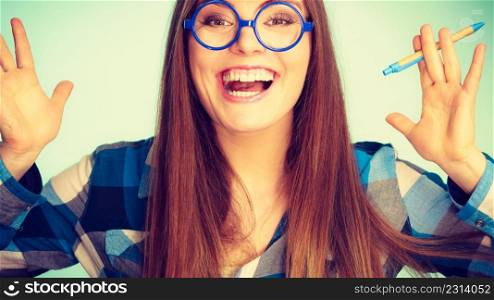 Studying, education and fun concept. Happy smiling nerdy thinking woman in weird big glasses having idea and holding pen. Studio shot on blue background. Happy nerdy woman in glasses holding pen