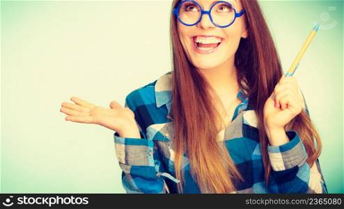 Studying, education and fun concept. Happy smiling nerdy woman in weird big glasses having idea and holding pen. Studio shot on blue background. Happy nerdy woman in glasses holding pen