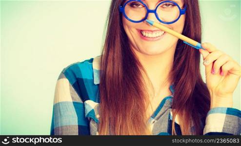 Studying, education and fun concept. Happy smiling nerdy woman in weird big glasses having idea and holding pen. Studio shot on blue background. Happy nerdy woman in glasses holding pen