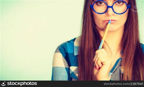 Studying, education and fun concept. Nerdy thinking woman in weird big glasses holding pen. Studio shot on blue background. Nerdy thinking woman in glasses holding pen