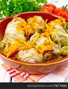 Stuffed cabbage meat in cabbage leaves with roasted carrots in a brown ceramic pan on a napkin, tomatoes, parsley on a light background boards