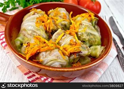 Stuffed cabbage meat in cabbage leaves with roasted carrots in a ceramic pan on a napkin, tomatoes, parsley on a lighter background board