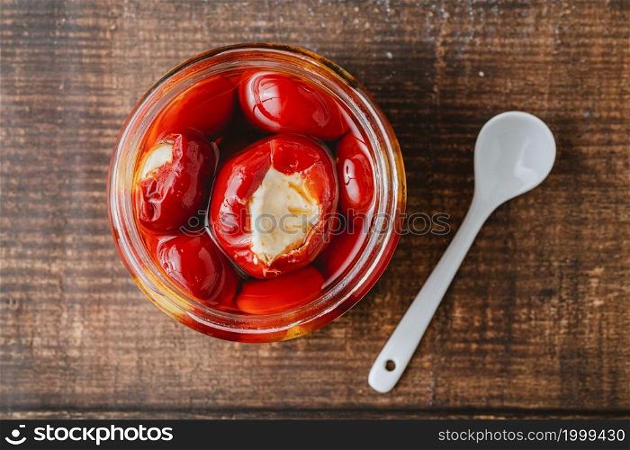 Stuffed cherry peppers with ricotta cheese filling in glass jar on wooden background