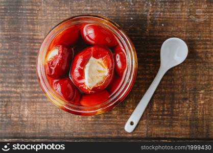 Stuffed cherry peppers with ricotta cheese filling in glass jar on wooden background