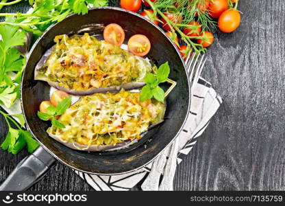 Stuffed eggplant with smoked brisket, tomatoes, onions, carrots with garlic, cheese and herbs in a pan on a napkin on black wooden board top