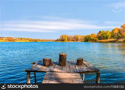 Stumps on old wooden fishing pier at sunny autumn day on river
