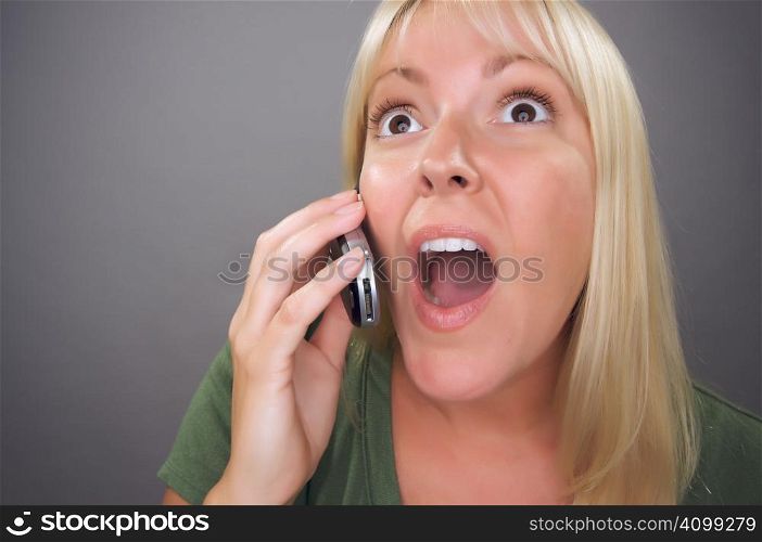 Stunned Blond Woman Using Cell Phone Against a Grey Background.