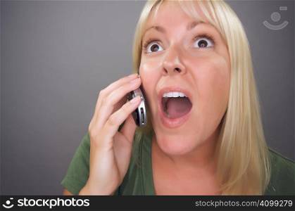 Stunned Blond Woman Using Cell Phone Against a Grey Background.