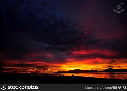 Stunning and colourful sunset with overcast sky over the Indian Ocean with silhouette of an island and reflection on the sea. Seychelles