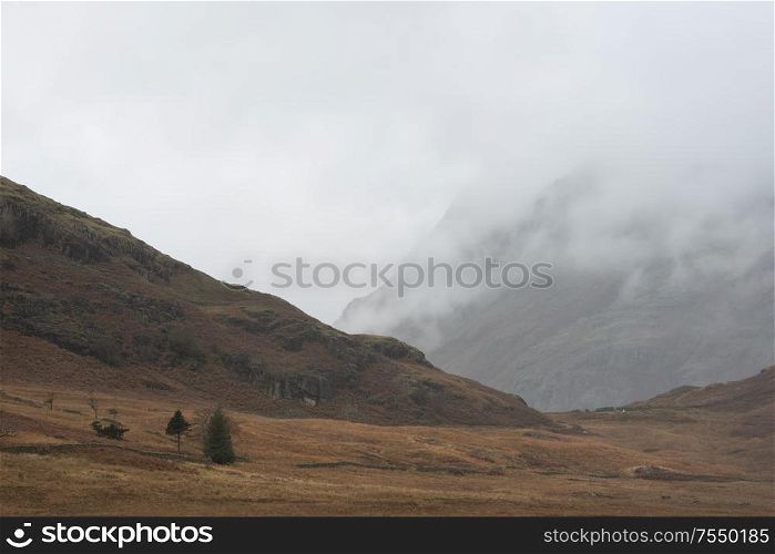 Stunning Autumn Fall landscape image of Langdale Pikes mountain range in Lake District in mist and low cloud