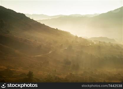 Stunning Autumn Fall landscape sunrise in the Lake District with sun beams streaming through the mist into The Langdales valley