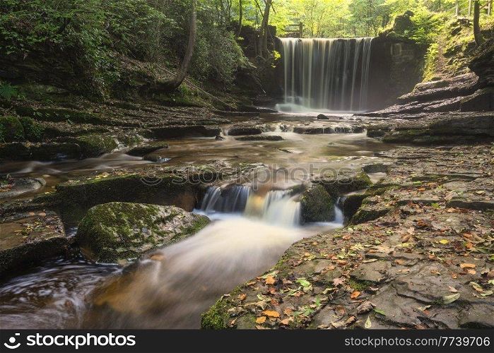 Stunning beautiful Autumn landscape image of Nant Mill waterfall in Wales with glowing sunlight through the woodland